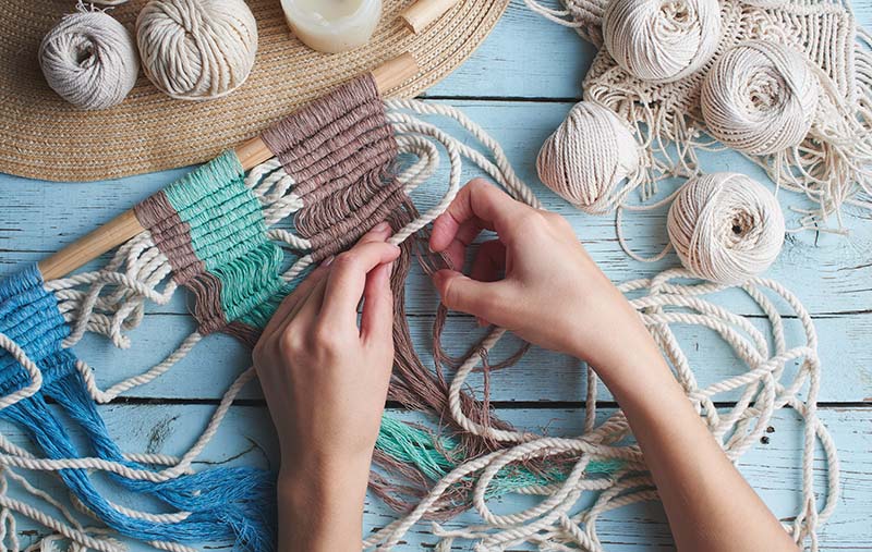 macrame supplies lie all over the table while someone works on their macrame project, which is 10% started