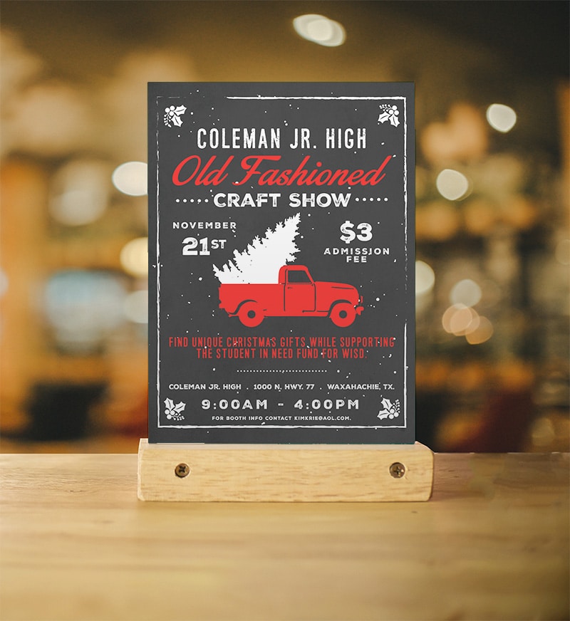 An event flyer sits in a blonde wooden perch on a blonde wooden table in front of light colored bokeh. The flyer is an eye catching design for the Coleman Jr High Old Fashioned Craft Show