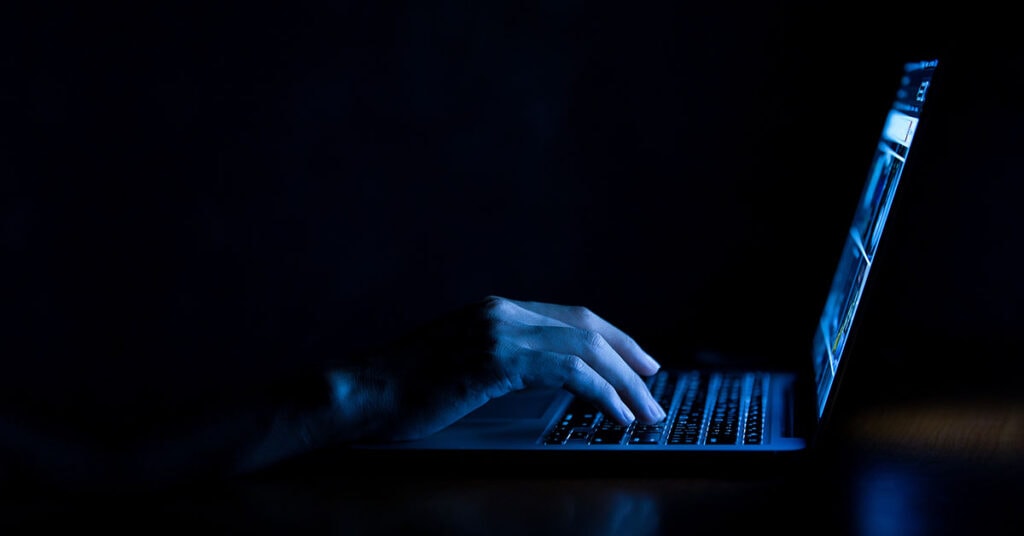 A room lit only by the computer screen reveals someone typing in the dark