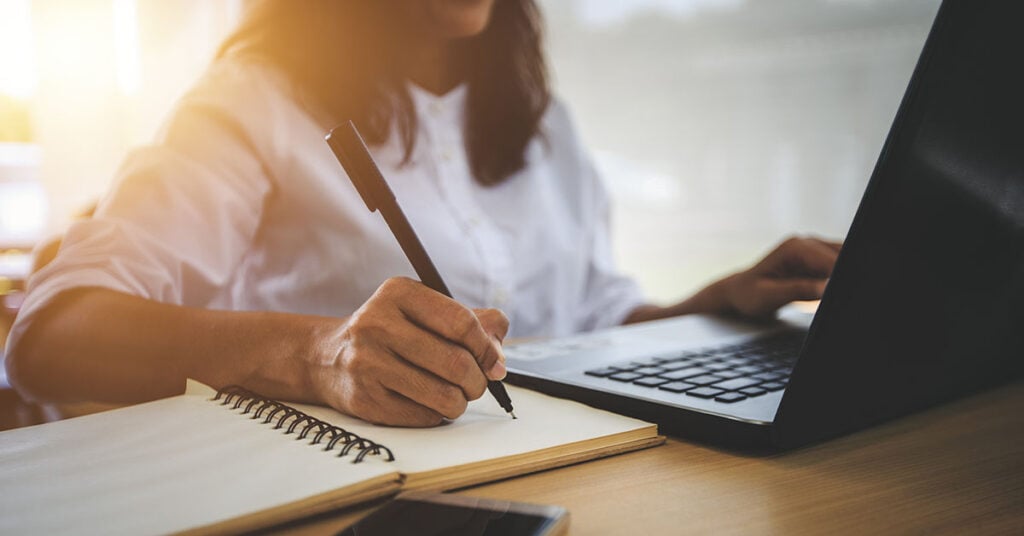 a person sits at their computer taking notes while browsing