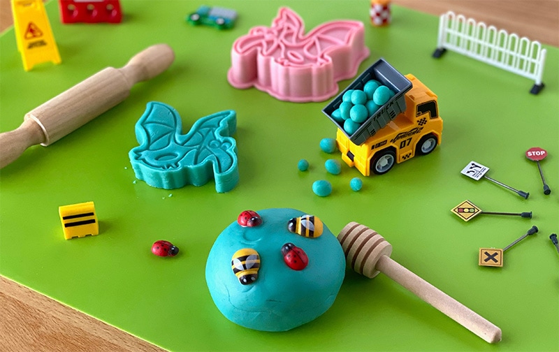 play dough in play surrounded by several toys and and tools from sensory kit like rolling pin, construction truck, street signs etc