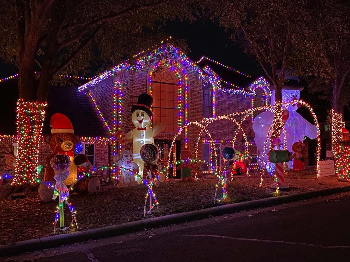 A house is lit up with christmas lights all along their driveway and christmas decor stands alongside