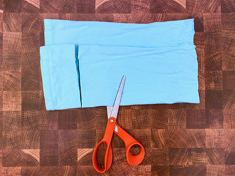 orange handled scissors are cutting through folded t-shirt fabric while leaving a gap uncut