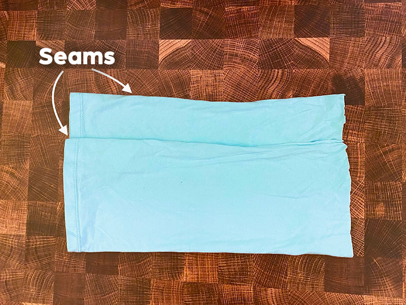 a cut shirt is folded over with the seams on the same side. There is text labeling both seams. One seam is about 2" lower than the other seam.