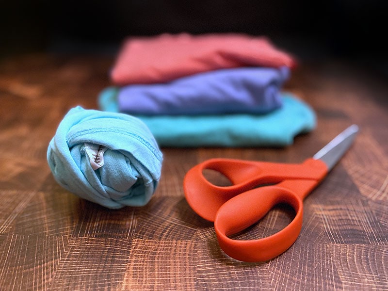 stack of folded t shirts sits behind a ball of t shirt yarn and scissors