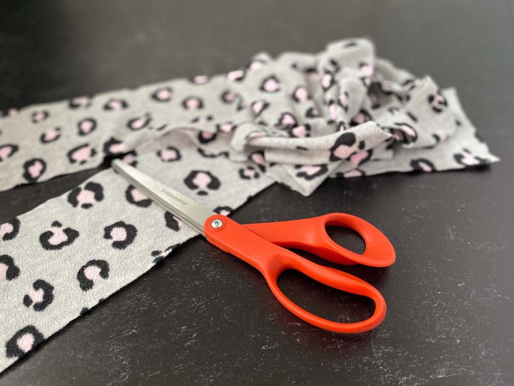 Strips of fleece fabric have been cut and sit next to orange handled scissors