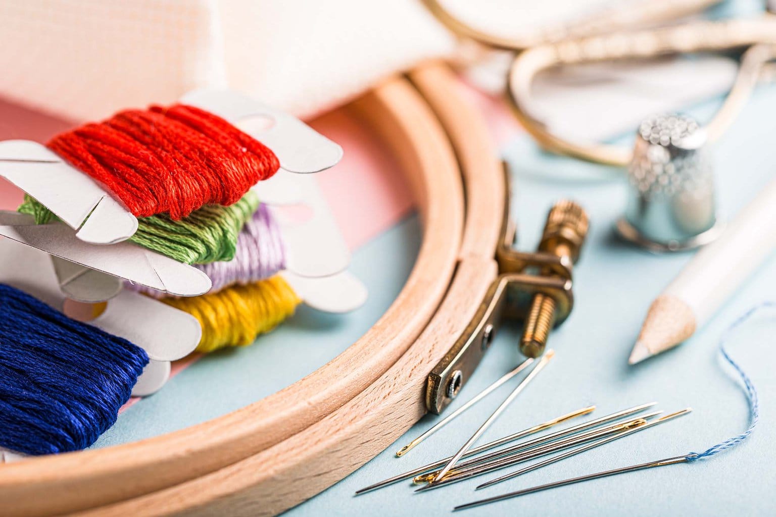 An embroidery hoop with carded floss and other kit supplies are laid out on a table