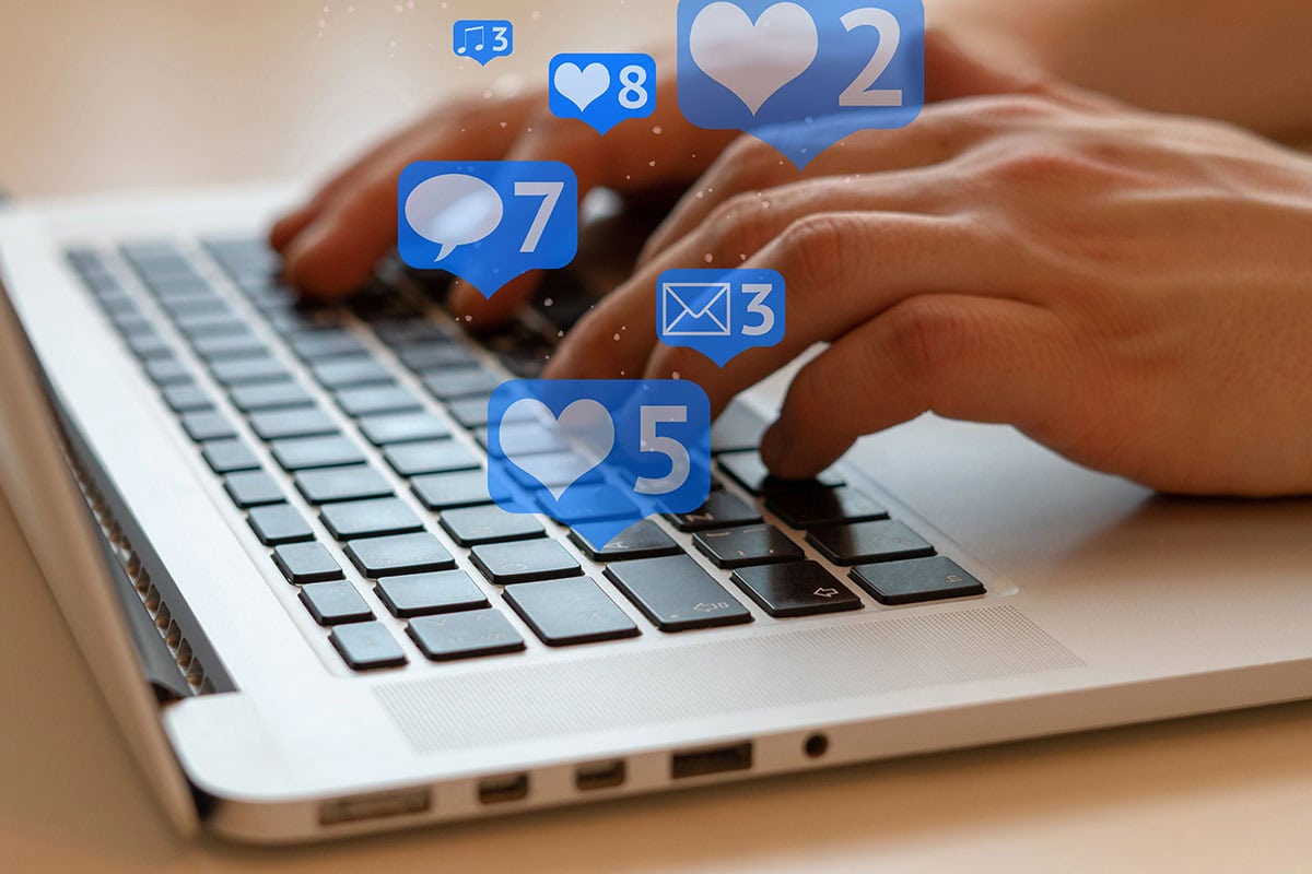A close up of someone typing on a keyboard with facebook like and react type icons floating around in blue bubbles