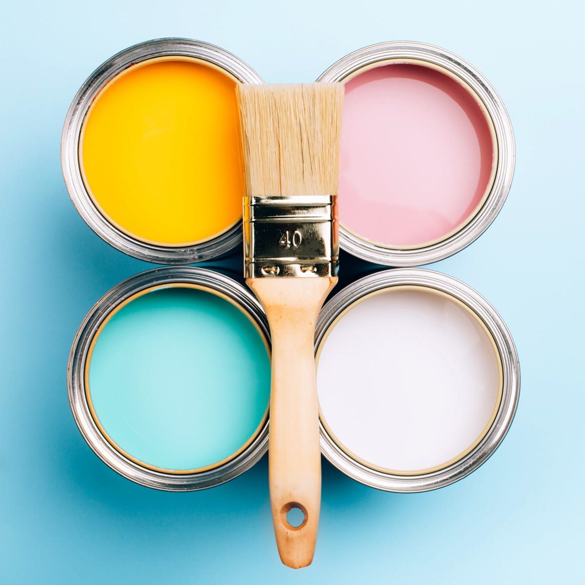 Four cans of paint (pink, yellow, blue, and white) are arranged in a square ontop a blue background. There is a large, clean, paint brush balanced in the middle of the cans of paint.